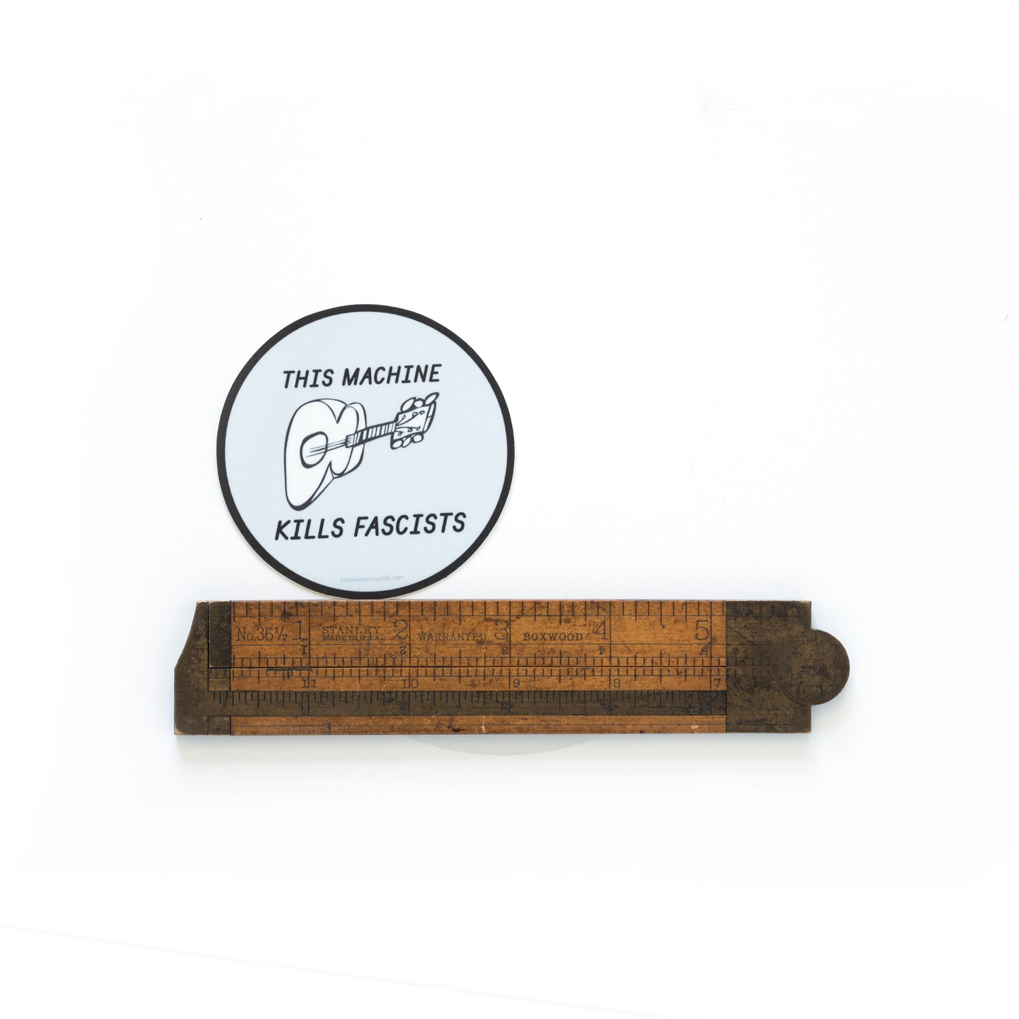 3-inch round vinyl sticker with “This Machine Kills Fascists” text — inspired by Woody Guthrie’s iconic message. Shot with a ruler to show scale.