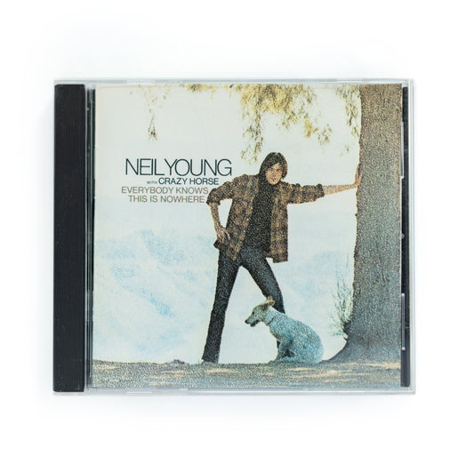 Front cover of Neil Young Everybody Knows This Is Nowhere CD featuring sepia-toned photo of Neil Young leaning against a tree with dog, classic 1969 Reprise Records release, includes 'Cinnamon Girl' and 'Down by the River,' folk rock and country rock icon.