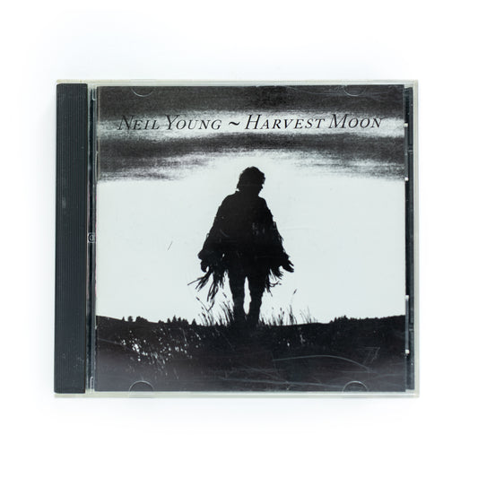 Neil Young – Harvest Moon CD album cover featuring an image of Neil Young against a twilight sky with a large moon in the background, showcasing the rustic and serene vibe of the album's country-folk sound.