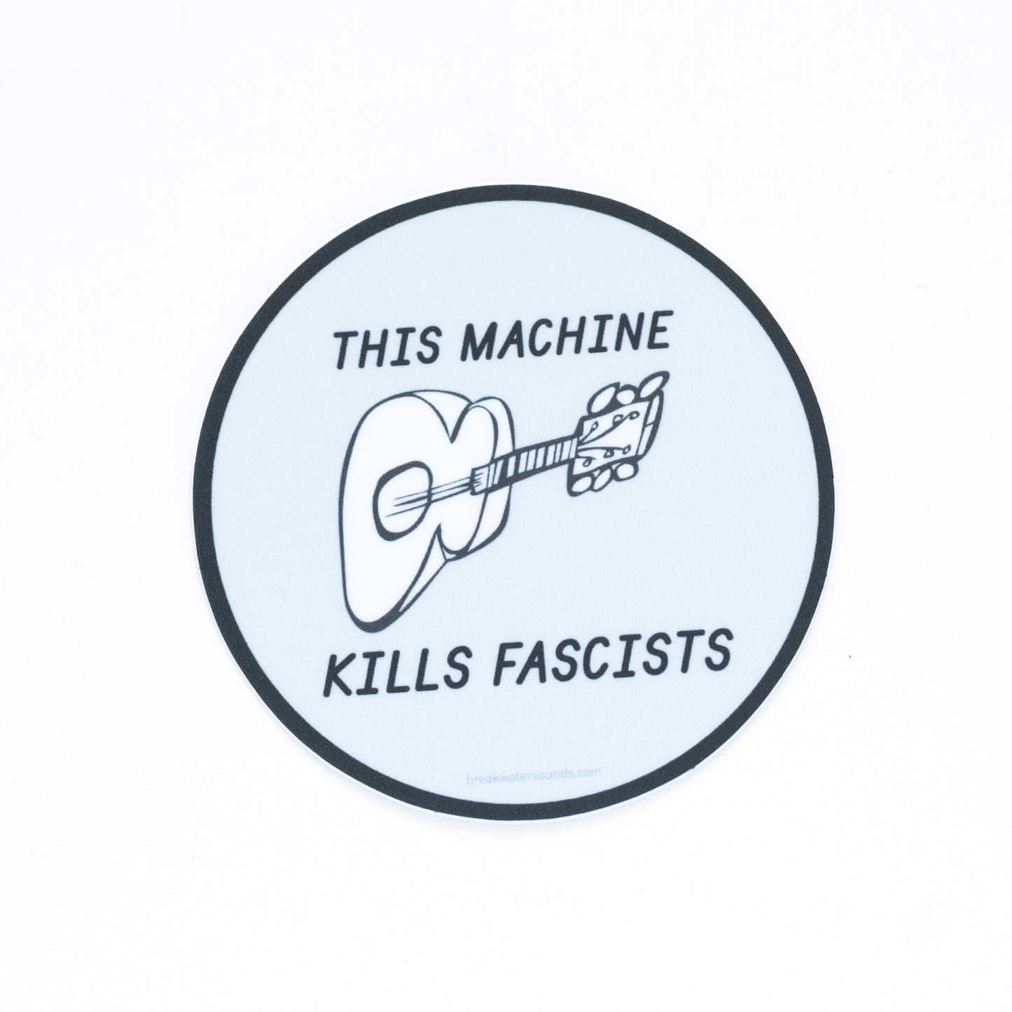 3-inch round vinyl sticker with “This Machine Kills Fascists” text — inspired by Woody Guthrie’s iconic guitar message — matte, waterproof, and UV coated. Features and illustration of a guitar. 

