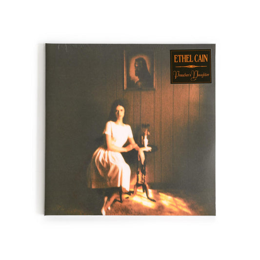 Ethel Cain – Preacher’s Daughter album cover featuring an out of focus image of Ethel against a wood panel background with a portrait of Jesus on the wall, evoking themes of American Gothic, grief, and lost innocence. Atmospheric and cinematic.