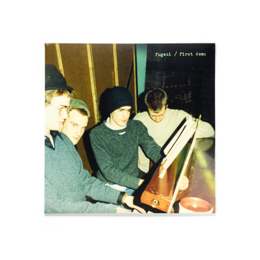 Fugazi - first demo LP front cover with a photograph of the band sitting at a piano. Ian MacKaye is looking at the camera while the rest of the band is not. 