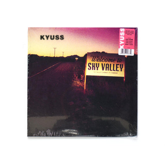 Kyuss Welcome To Sky Valley front cover featuring a dusk-lit desert road sign reading "Sky Valley" against a purple and orange sky.